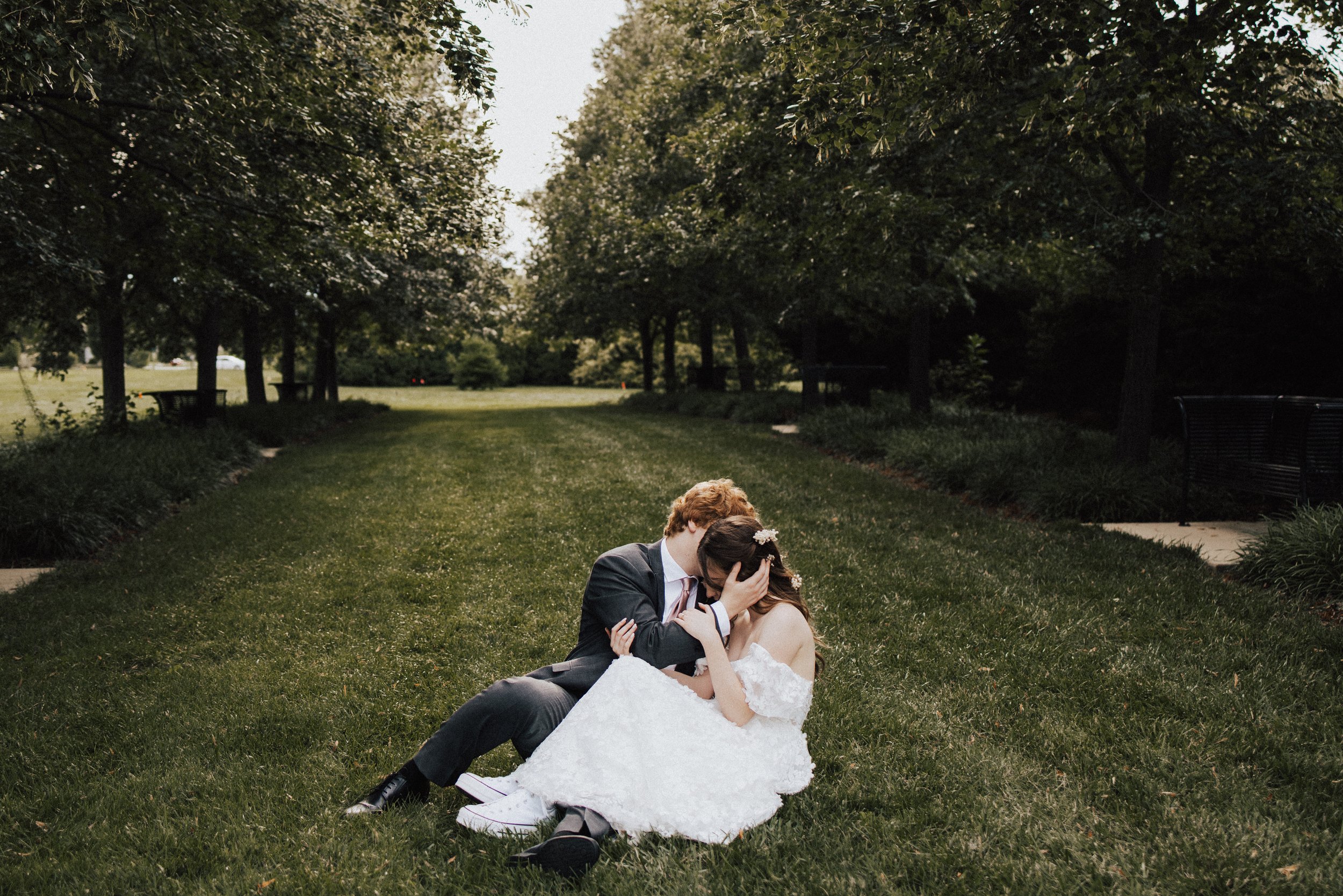 Bride and Groom sitting in grass, tangled in each other surrounded by beautiful trees.